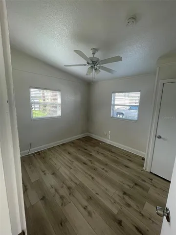 an empty room with wooden floor fan and windows
