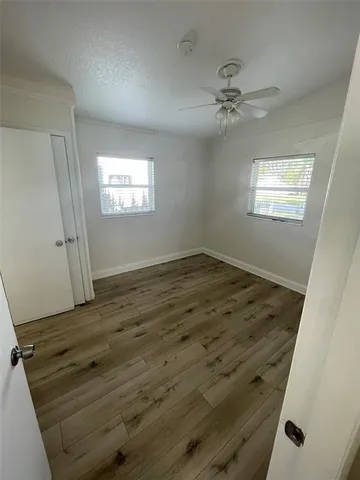 an empty room with wooden floor fan and windows