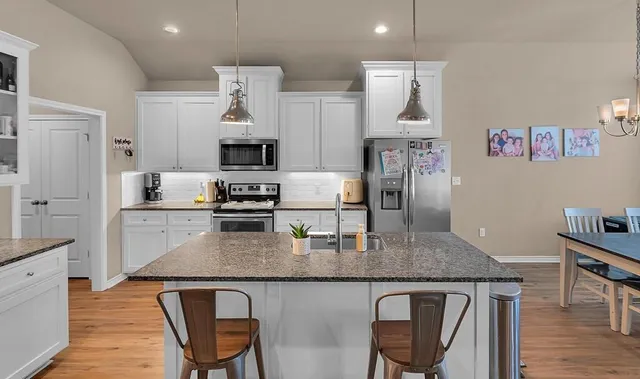 a kitchen with kitchen island granite countertop a table chairs refrigerator and microwave