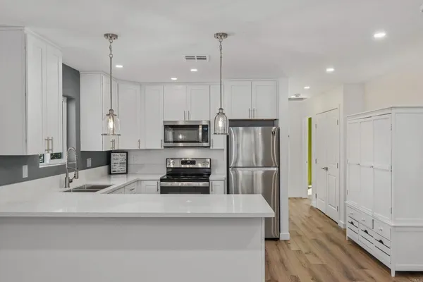 a kitchen with stainless steel appliances a refrigerator stove microwave and white cabinets with wooden floor