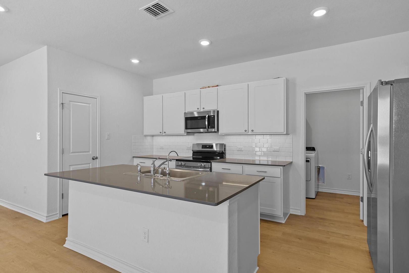 A well-lit kitchen presents a functional island with a sink and ample counter space for culinary endeavors.
