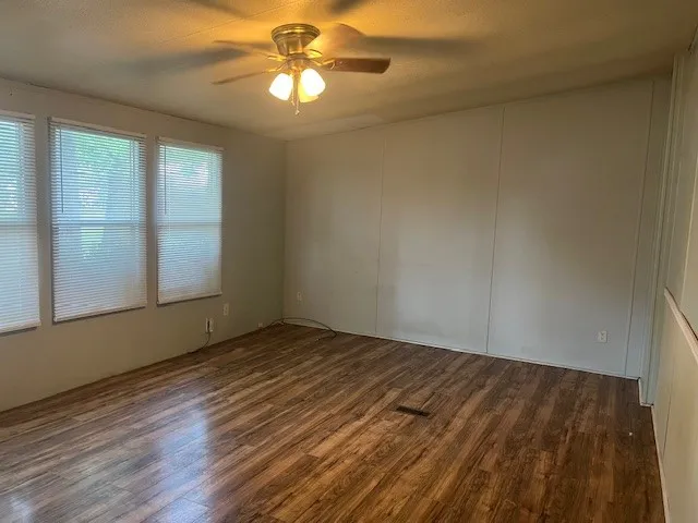 an empty room with wooden floor chandelier fan and windows