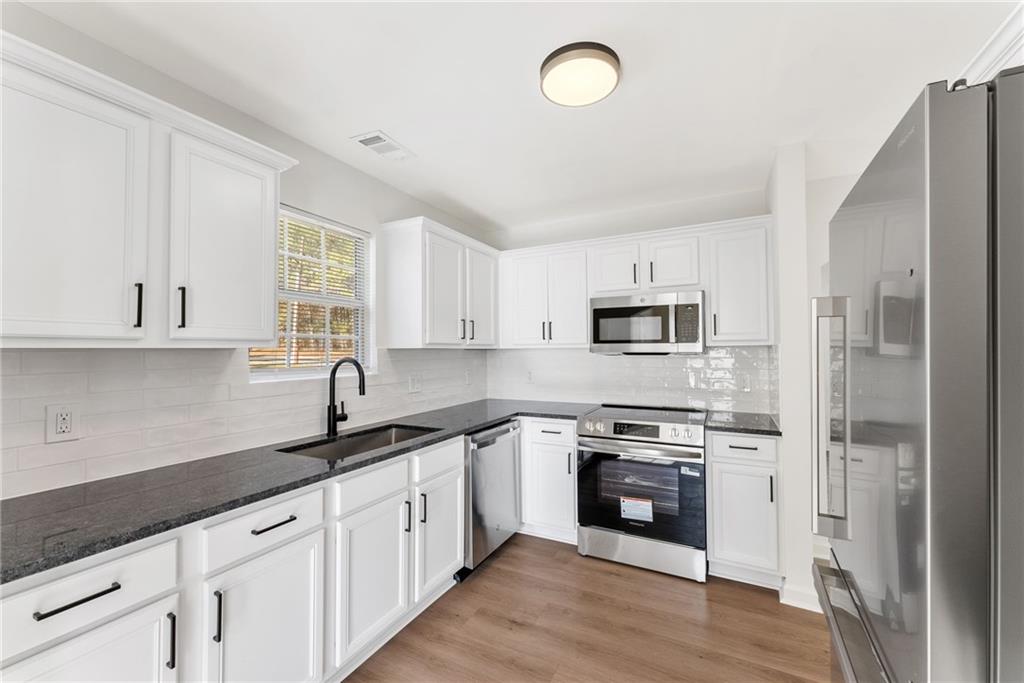 5805 Marbut Road Lithonia, GA 30058 - Photo 20 of 46 a kitchen with stainless steel appliances granite countertop a sink a stove a refrigerator and white cabinets with wooden floor