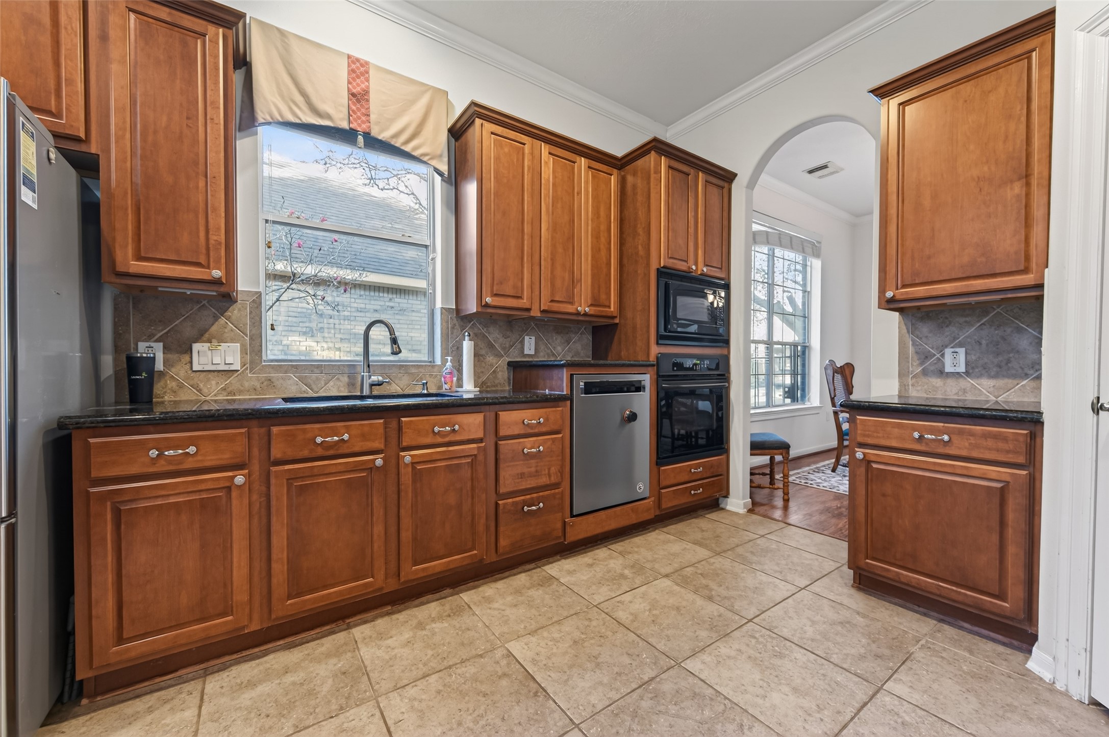 27 Sovereign Way Conroe, TX 77384 - Photo 16 of 49 This kitchen features warm wooden cabinets, sleek black countertops, and tiled backsplash. A large window above the sink offers natural light.