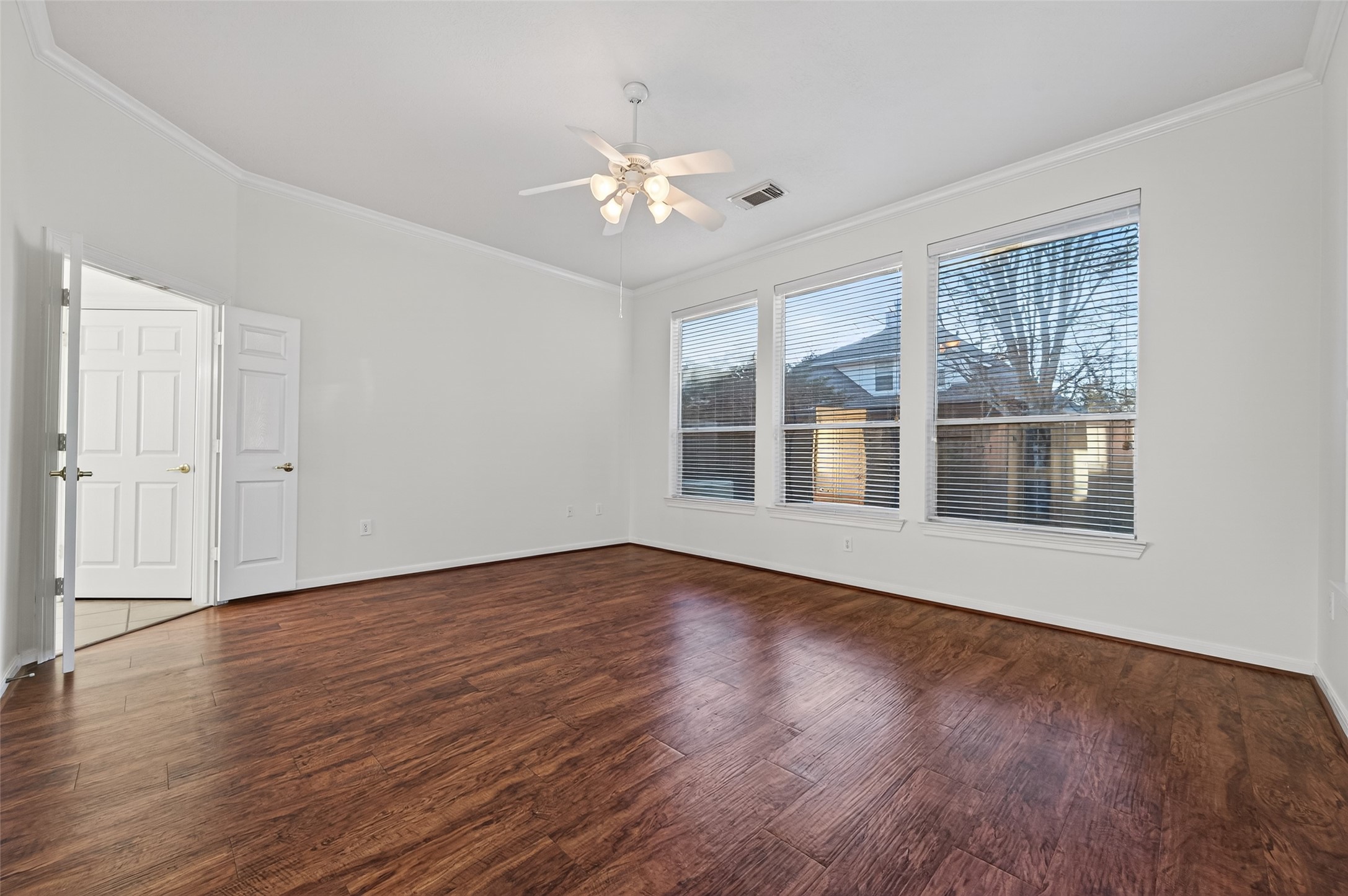 27 Sovereign Way Conroe, TX 77384 - Photo 20 of 49 Bright, spacious primary bedroom with large windows, hardwood floors, and a ceiling fan.