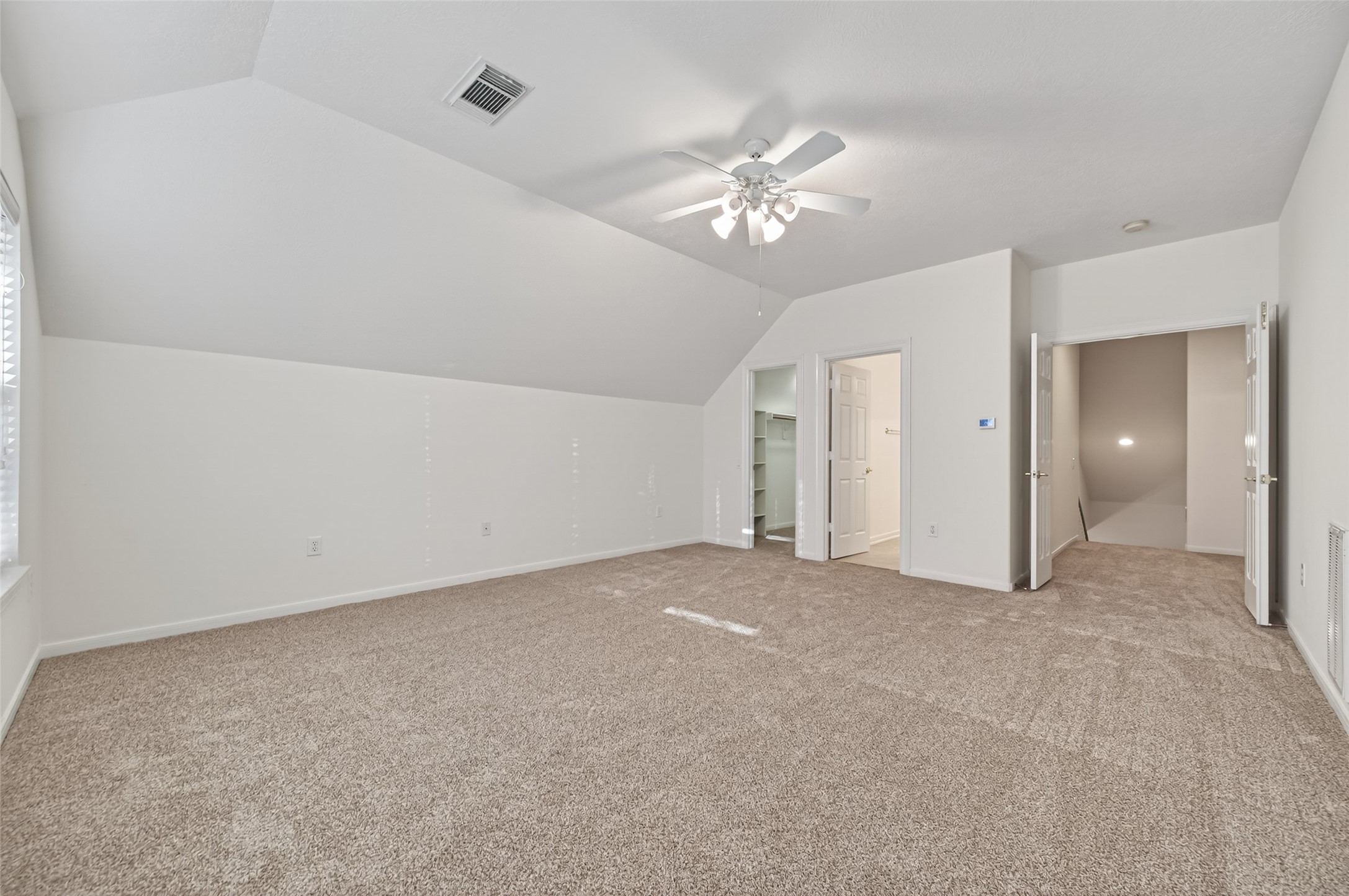 27 Sovereign Way Conroe, TX 77384 - Photo 28 of 49 This spacious room features neutral carpeting, a ceiling fan, and sloped ceilings. It includes a walk-in closet and an adjacent bathroom, offering ample storage and versatile space.