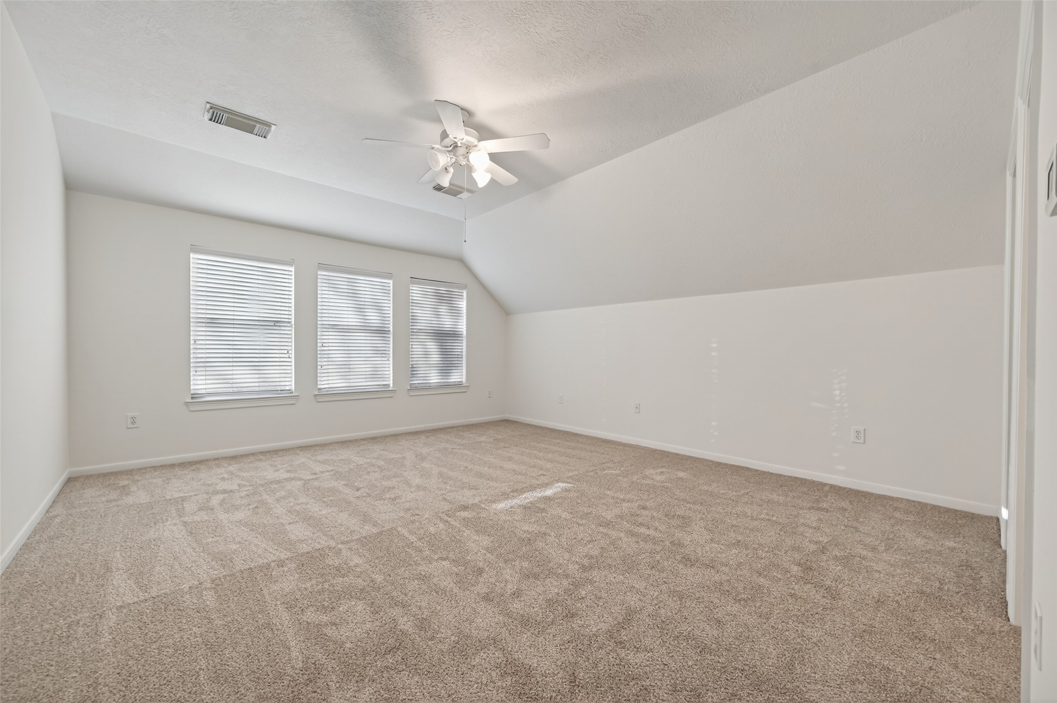 27 Sovereign Way Conroe, TX 77384 - Photo 29 of 49 This room features neutral carpet and walls, with a sloped ceiling and a ceiling fan. Natural light streams in through three large windows.