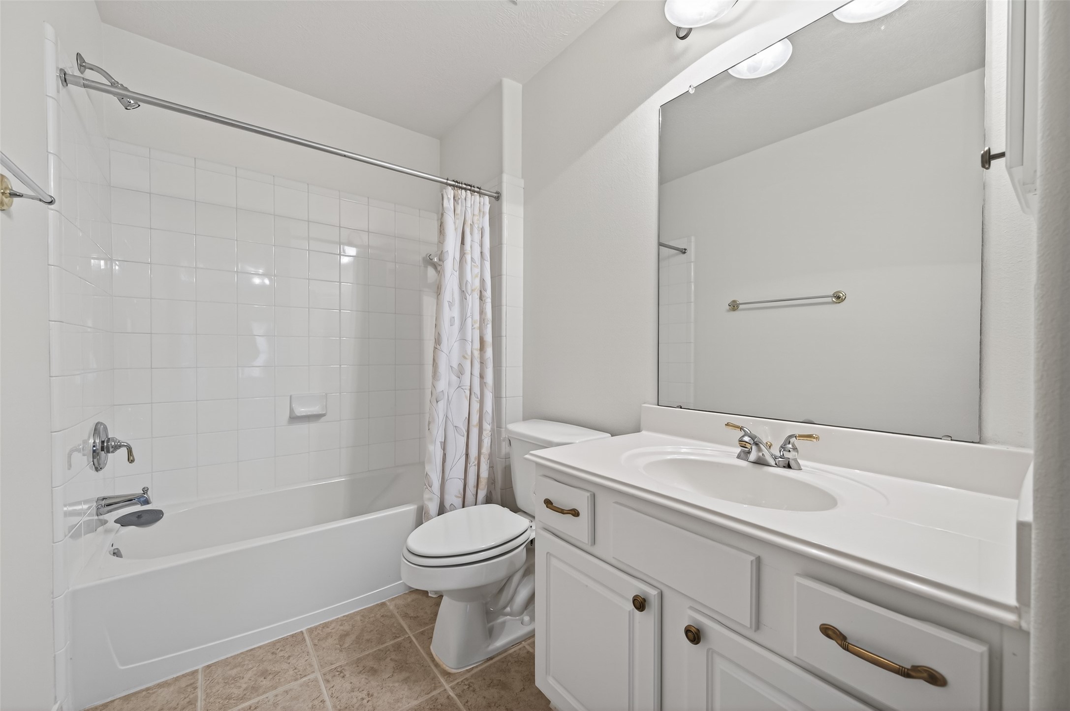 27 Sovereign Way Conroe, TX 77384 - Photo 30 of 49 This bathroom features a clean, white design with a combined shower and bathtub, a large mirror above a vanity with storage, and neutral tile flooring.