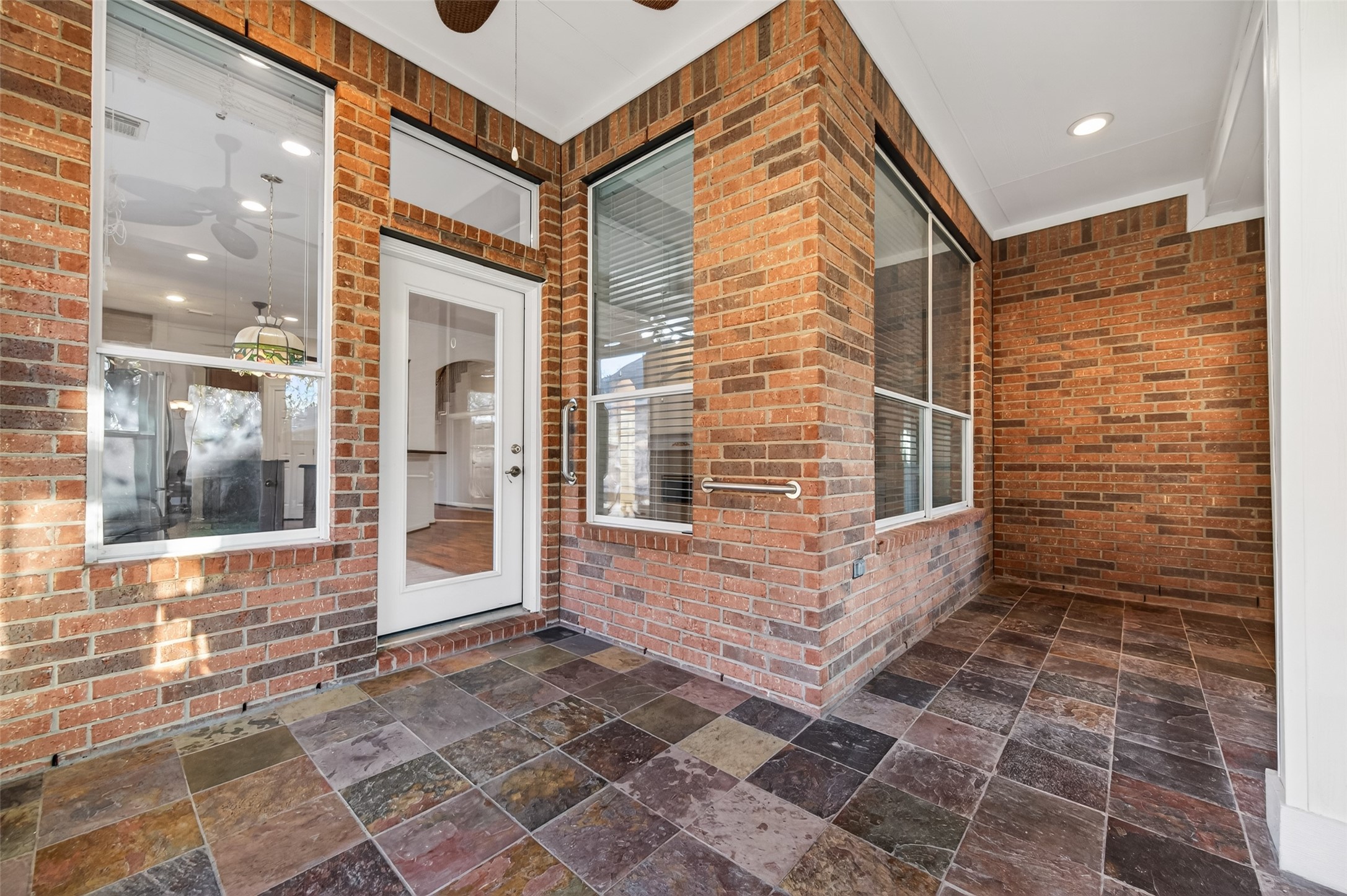 27 Sovereign Way Conroe, TX 77384 - Photo 31 of 49 This photo showcases a cozy, covered sunroom area with brick walls and a slate tile floor. Large windows and a glass door offer natural light and a view into the interior, creating a seamless indoor-outdoor connection.