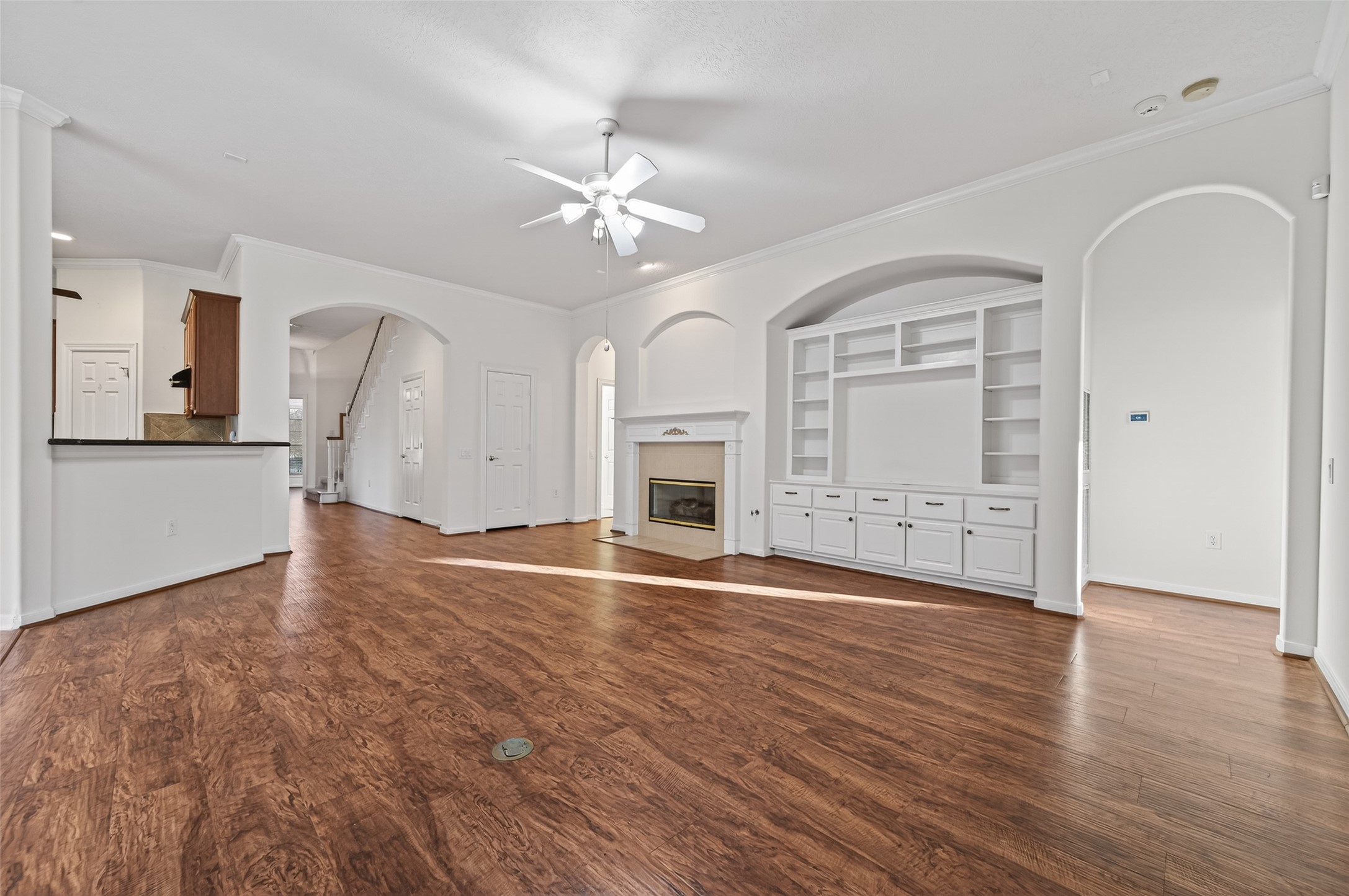 27 Sovereign Way Conroe, TX 77384 - Photo 9 of 49 Bright and spacious living room with hardwood floors, built-in shelving, and a cozy fireplace. The open layout connects to the kitchen, featuring ample natural light and a ceiling fan for comfort.