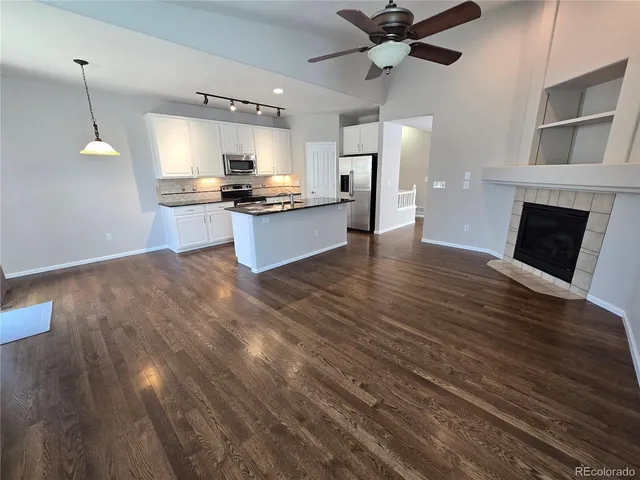 a view of kitchen and empty room with wooden floor and fan