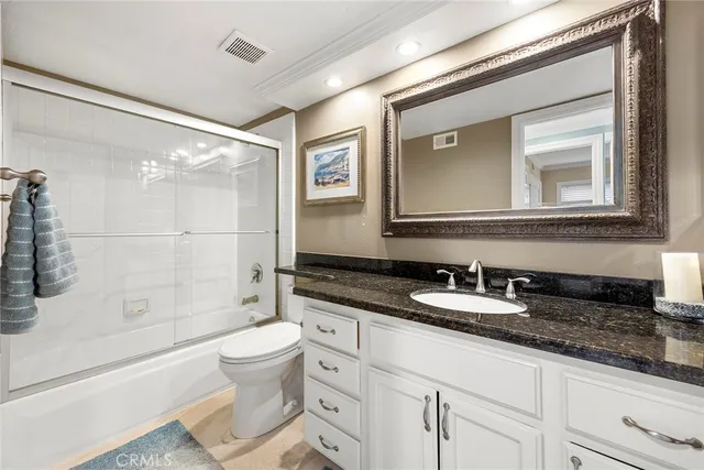 a bathroom with a granite countertop sink a toilet a mirror and shower