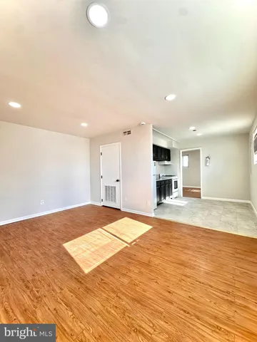 a view of empty room with wooden floor and kitchen view