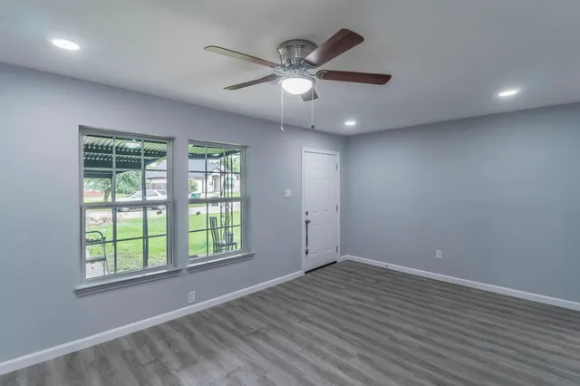 an empty room with wooden floor chandelier fan and windows