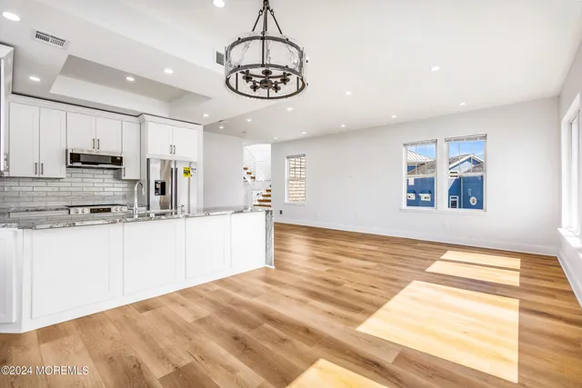 a view of a kitchen with stainless steel appliances granite countertop a stove a sink dishwasher and white cabinets with wooden floor