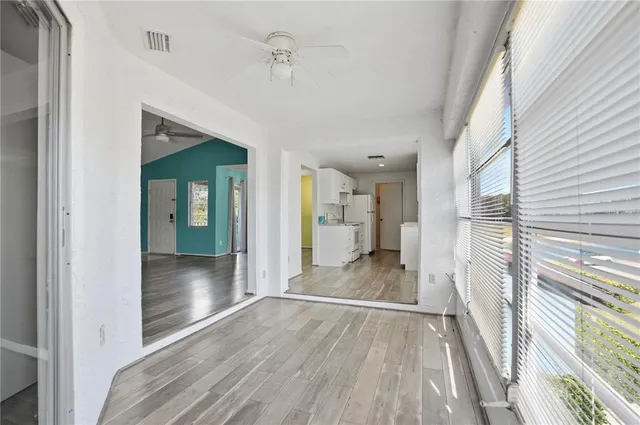 an empty room with wooden floor a ceiling fan and windows