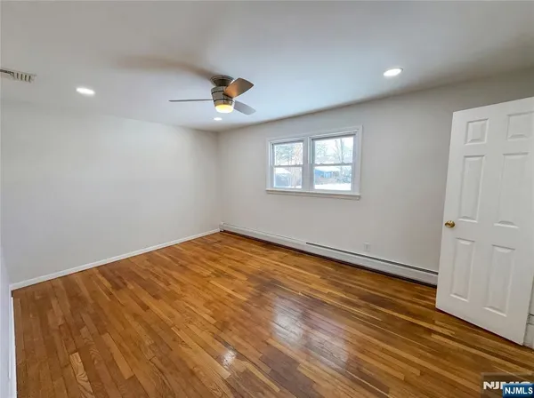 an empty room with wooden floor ceiling fan and windows