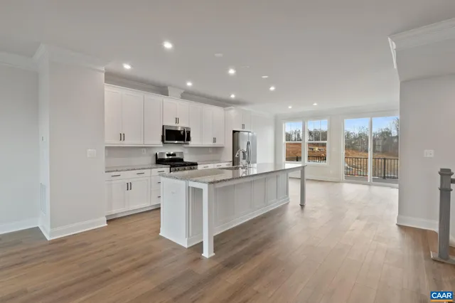 a kitchen with stainless steel appliances granite countertop a stove top oven a sink a refrigerator and white cabinets with wooden floor