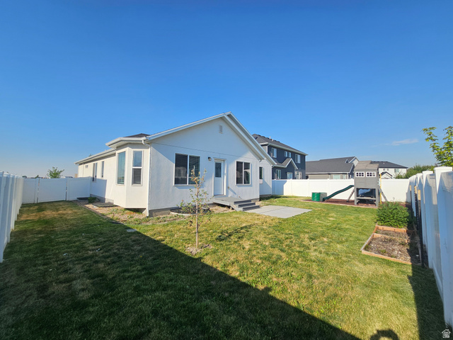 2508 Sunset Way Layton, UT 84041 - Photo 18 of 35 Expansive backyard featuring a manicured lawn, white privacy fencing, a concrete patio area, a bay window, and a rear entry door