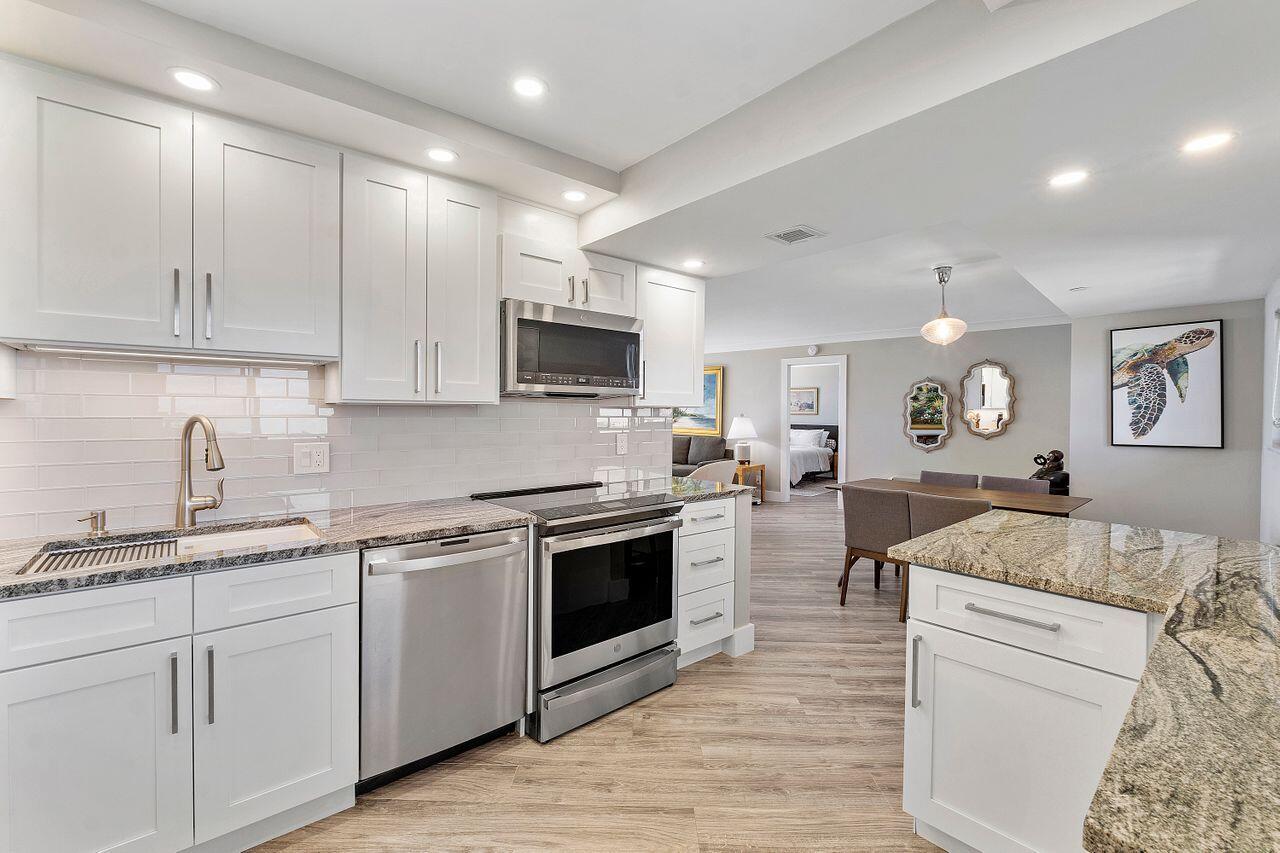 200 Ocean Trail Way, Unit 602 Jupiter, FL 33477 - Photo 14 of 50 a kitchen with stainless steel appliances granite countertop a sink dishwasher stove and white cabinets with wooden floor