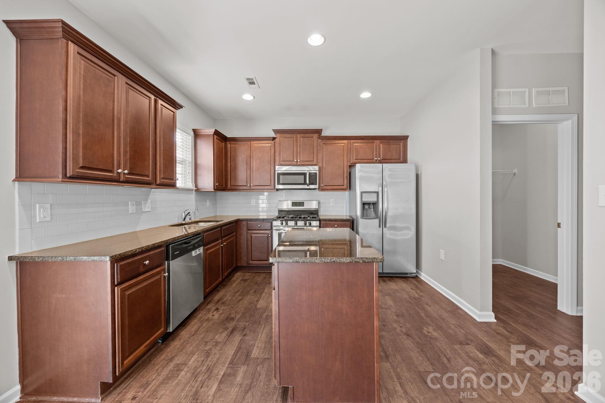 116 Rippling Water Drive Mount Holly, NC 28120 - Photo 14 of 48 a kitchen with stainless steel appliances granite countertop wooden cabinets a refrigerator a stove a sink and a microwave oven with wooden floor