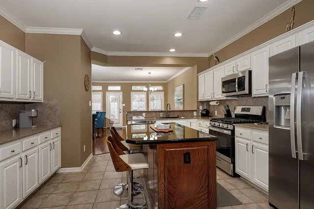 a kitchen with stainless steel appliances granite countertop a stove top oven a sink dishwasher a refrigerator and white cabinets with wooden floor