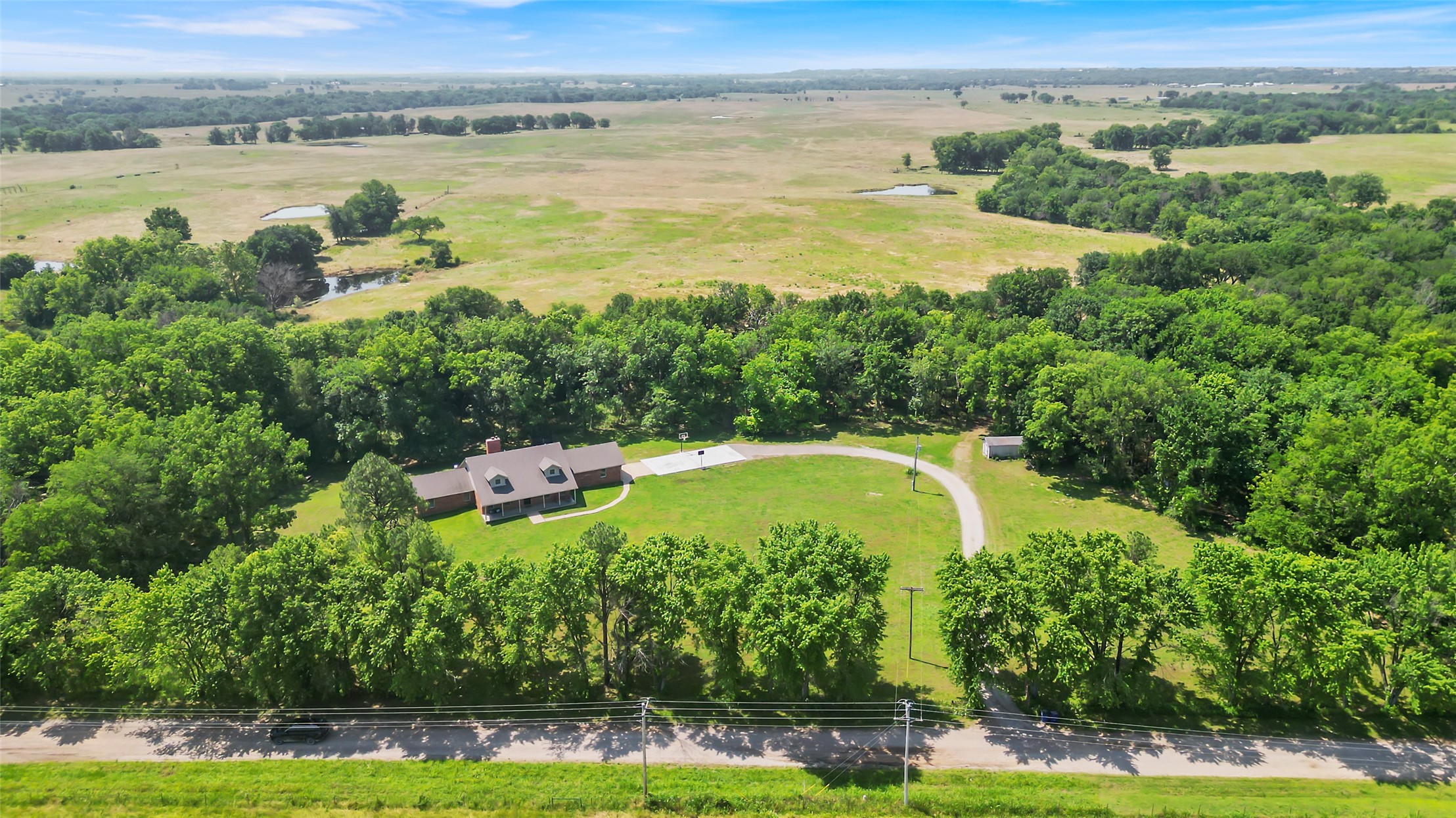 9644 19th Road Nowata, OK 74048 - Photo 32 of 36 Expansive property featuring a single-story residence with a front porch, a detached outbuilding, a curved driveway, and a natural pond