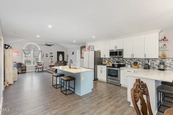 a open kitchen with stainless steel appliances kitchen island granite countertop a stove top oven a sink a dining table and chairs with wooden floor