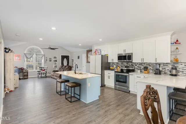 a open kitchen with stainless steel appliances kitchen island granite countertop a stove top oven a sink a dining table and chairs with wooden floor