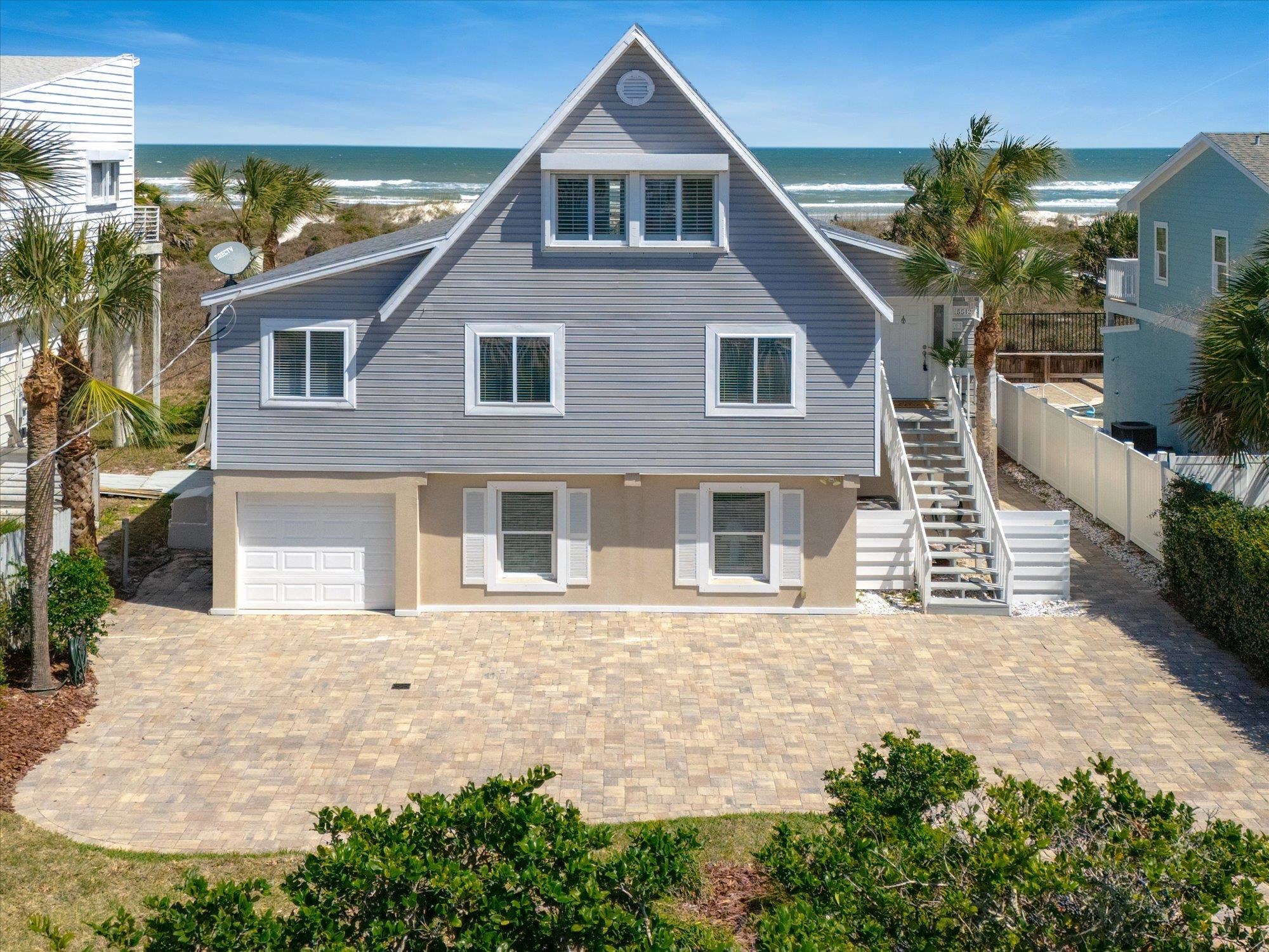 View of front facade with view of water and beach, a garage, decorative driveway, and a patio area
