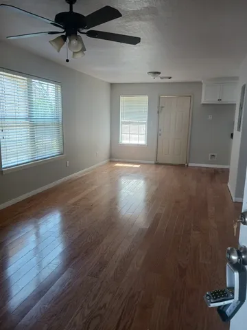 an empty room with wooden floor fan and windows