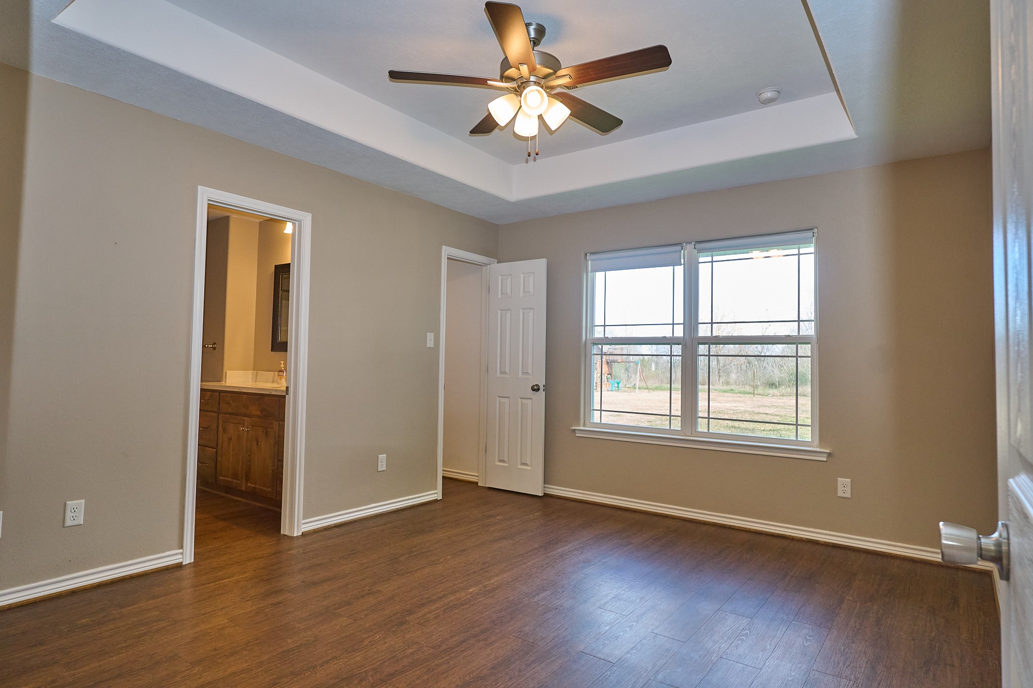 1807 Nuches Lane Bryan, TX 77803 - Photo 13 of 27 This photo showcases a bright, unfurnished room with wood flooring, a ceiling fan, and a large window providing ample natural light. The room connects to a bathroom, featuring a vanity area. The neutral wall colors offer a modern and versatile backdrop.