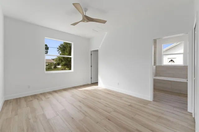 an empty room with wooden floor a ceiling fan and windows