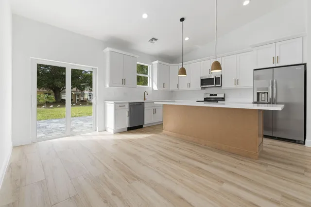 a open kitchen with kitchen island a stove a refrigerator wooden floor and a view of living room