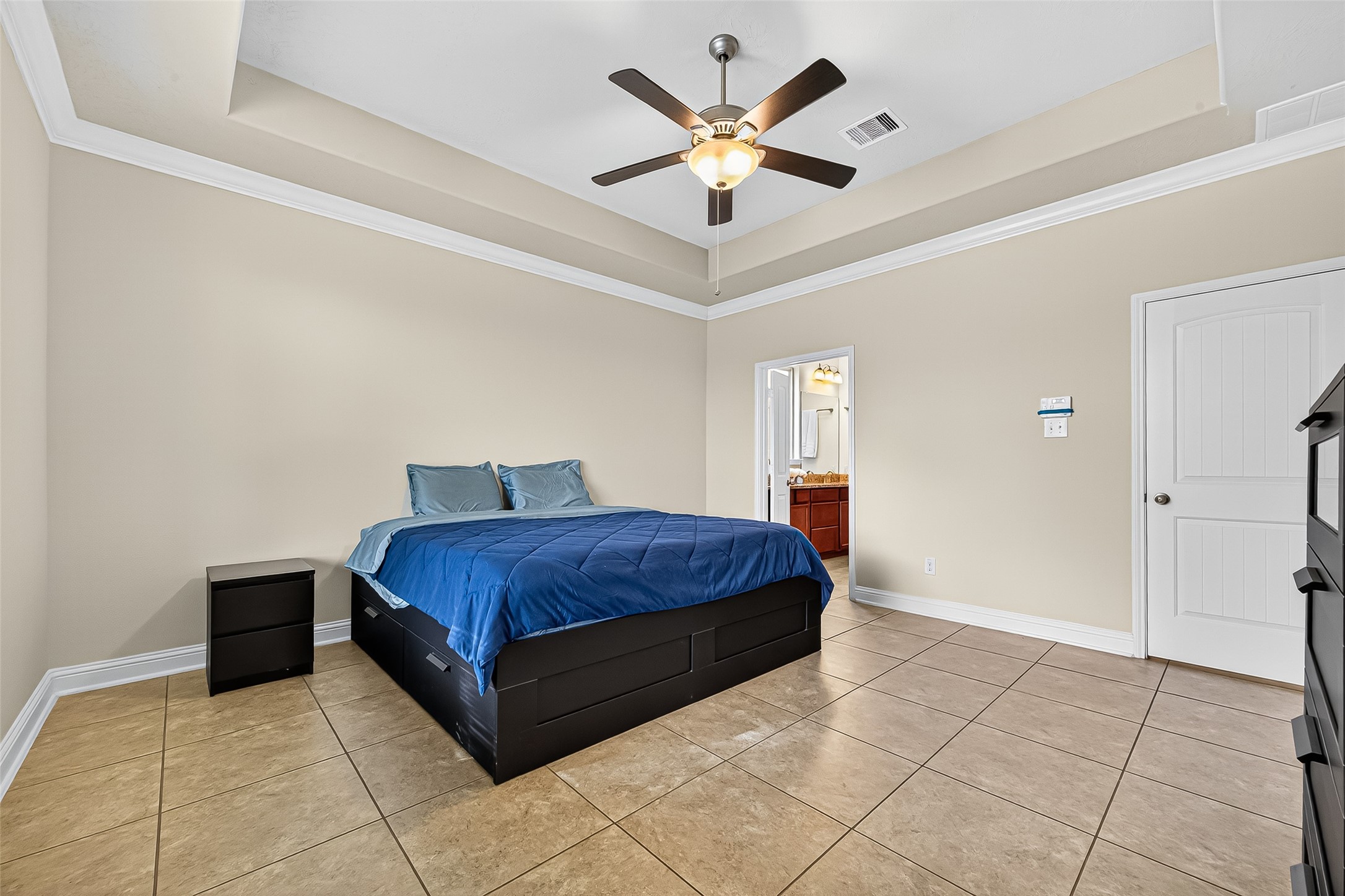 8107 Lockridge Terrace Lane Cypress, TX 77433 - Photo 29 of 50 Another view of the primary bedroom highlights the elegant tray ceiling with crown molding and a modern ceiling fan. The space feels grand yet peaceful, with warm tile flooring and a seamless flow into the en-suite bath—perfectly combining comfort and function.