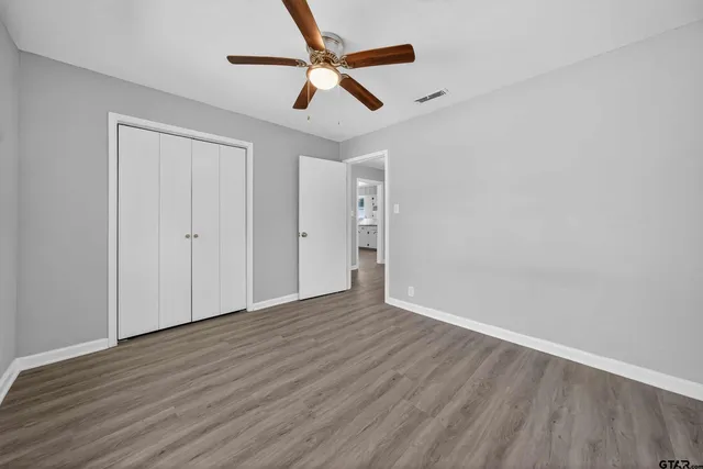 an empty room with wooden floor ceiling fan and windows