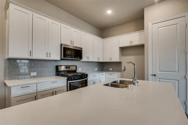 a kitchen with granite countertop a stove a sink and a white cabinets