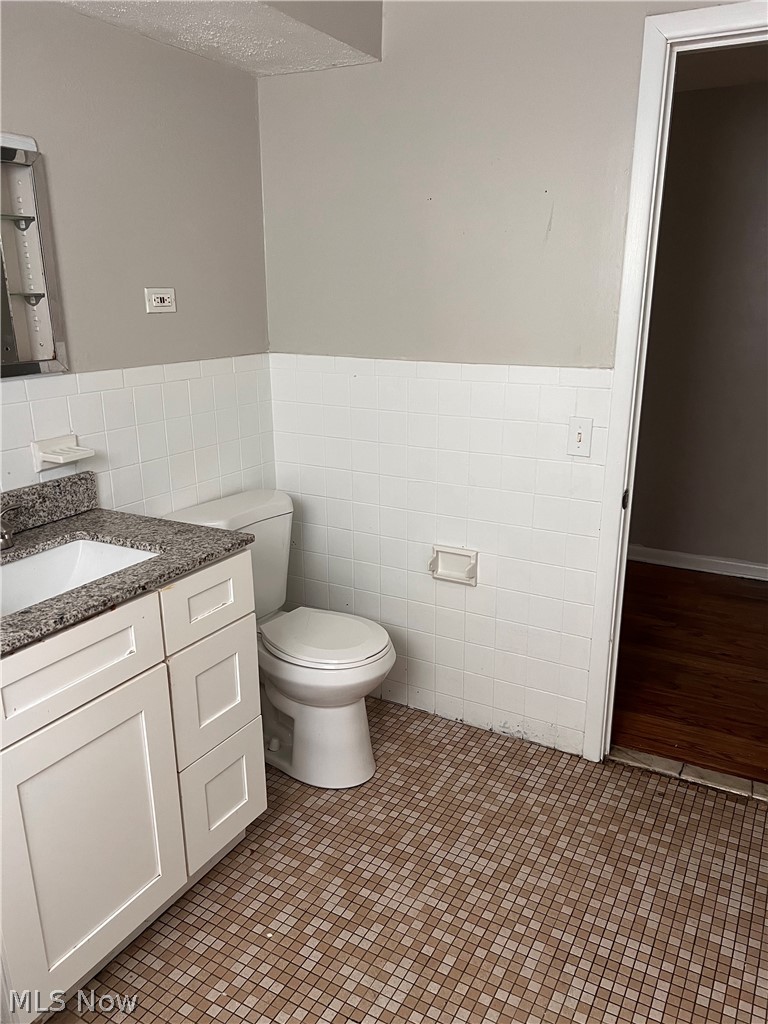 16350 Rockside Road Maple Heights, OH 44137 - Photo 15 of 34 Bathroom featuring a white vanity with a dark speckled countertop, mosaic tile flooring, white subway tile wainscoting, and a standard toilet