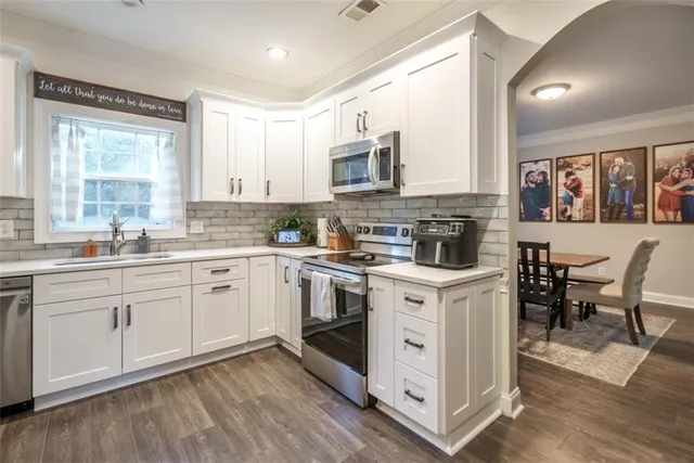 a kitchen with stainless steel appliances granite countertop a stove top oven a sink dishwasher and white cabinets with wooden floor
