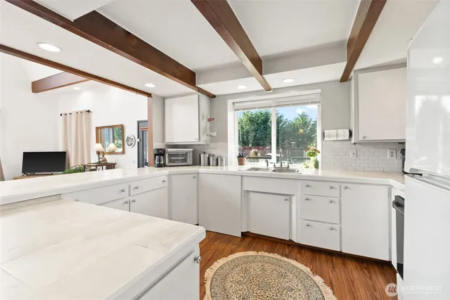 a kitchen with granite countertop white cabinets white appliances a sink and a large window