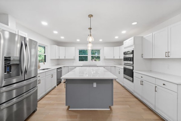 a kitchen with stainless steel appliances kitchen island granite countertop a refrigerator a sink dishwasher a oven and white cabinets with wooden floor