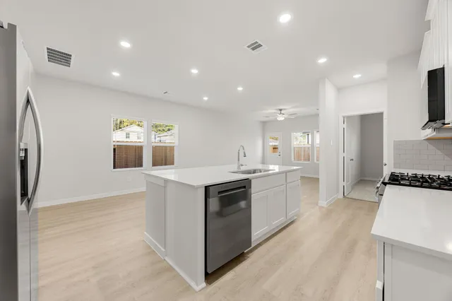 a kitchen with kitchen island granite countertop a stove top oven a sink dishwasher and a refrigerator with wooden floor