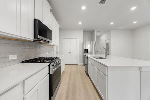 a kitchen with stainless steel appliances a sink stove top oven and white cabinets