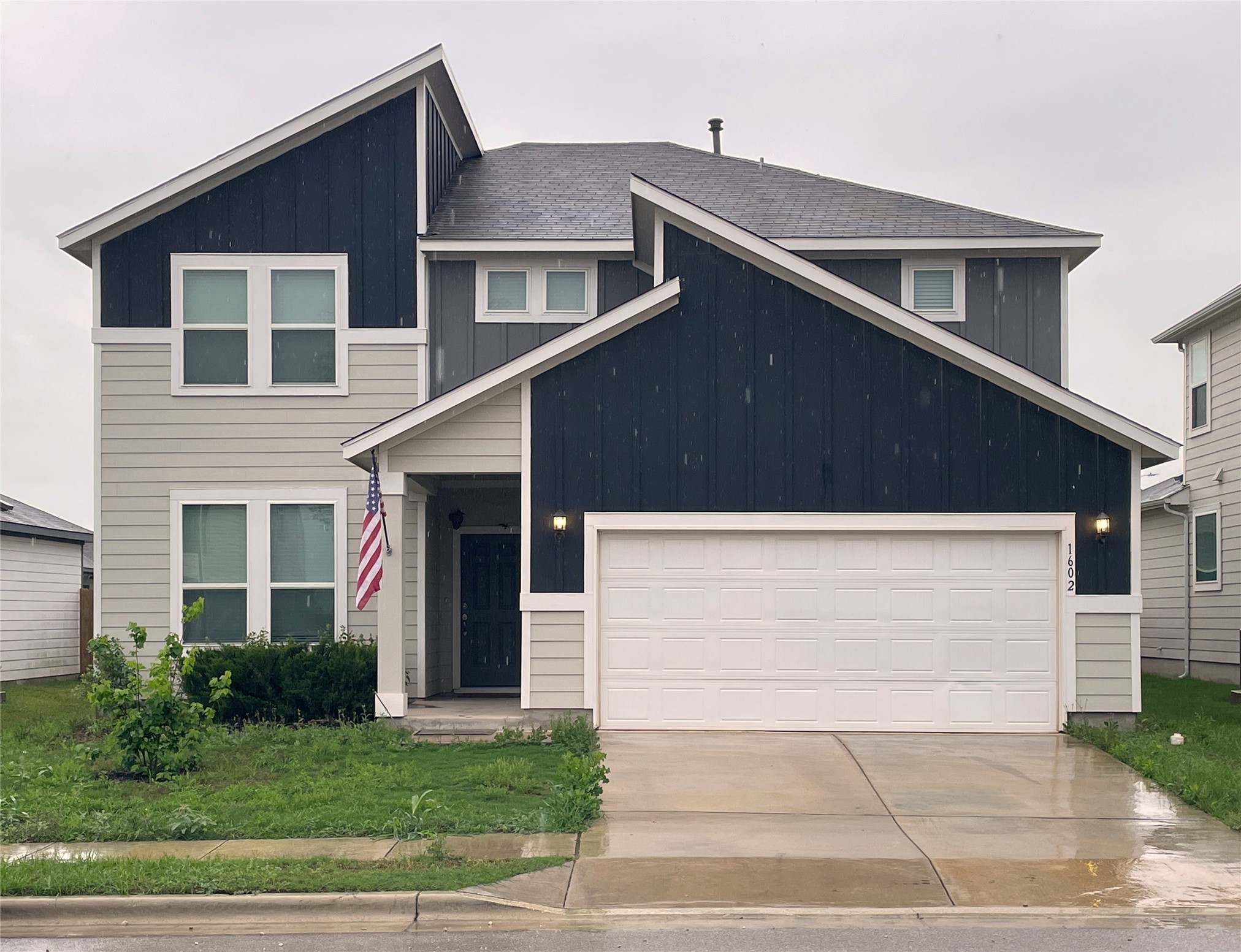 Contemporary two-story residence featuring a two-tone facade with contrasting siding, multiple window configurations, an attached two-car garage, and a covered front entry