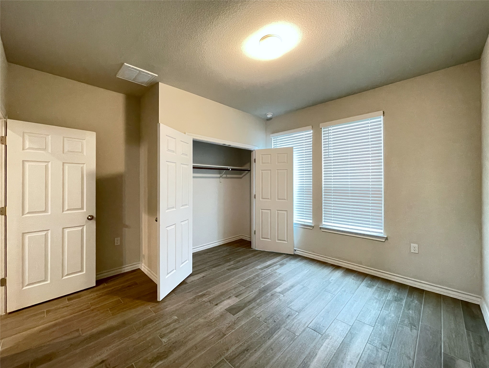 1602 Jacey Way Austin, TX 78725 - Photo 11 of 33 Spacious room featuring wood-finish flooring, two windows with blinds, a bi-fold closet with shelving and hanging rods, a flush-mount ceiling light, and neutral wall paint