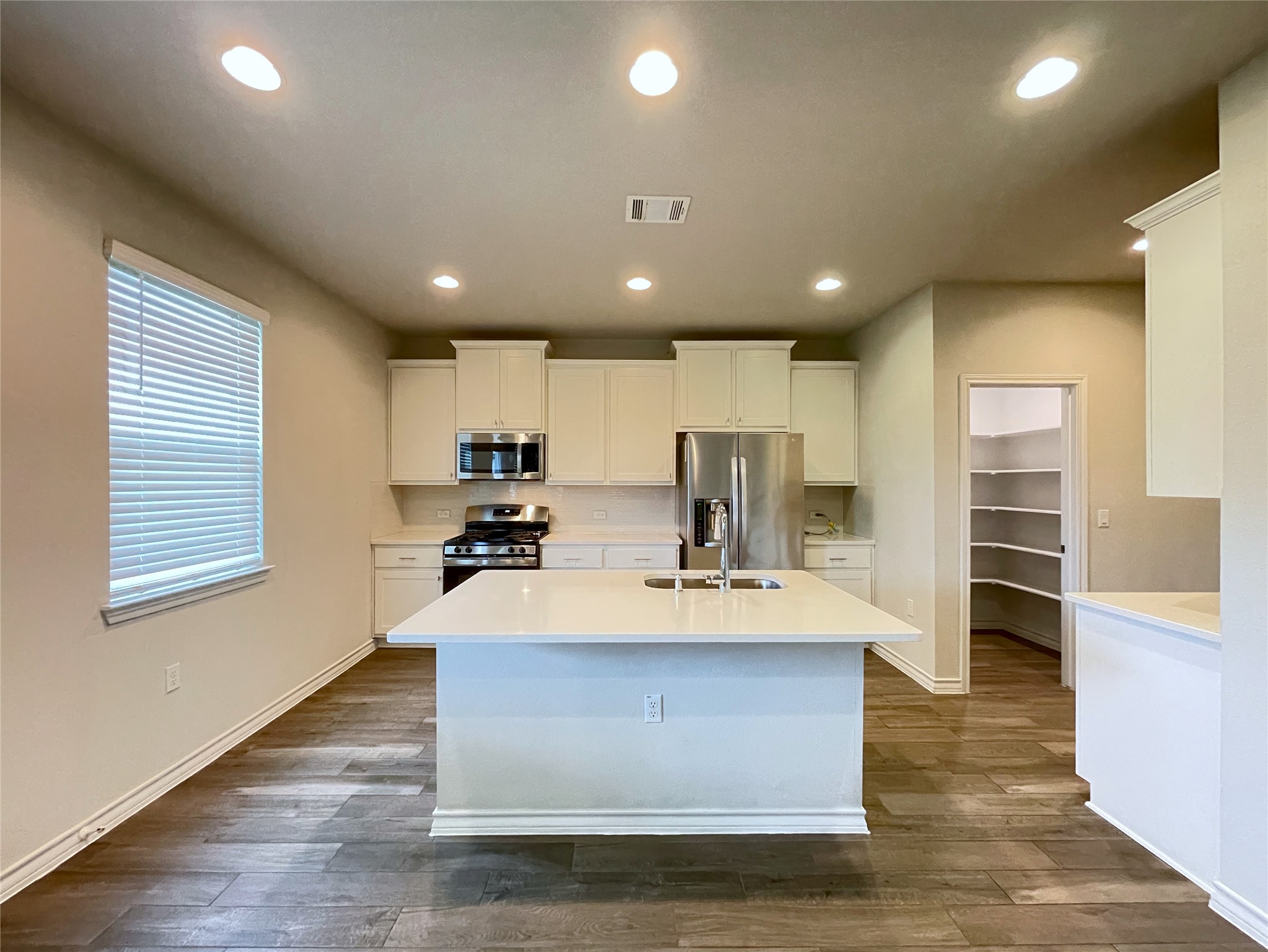 1602 Jacey Way Austin, TX 78725 - Photo 5 of 33 Kitchen featuring a large central island with a sink, stainless steel appliances, white cabinetry, and wood-finish flooring