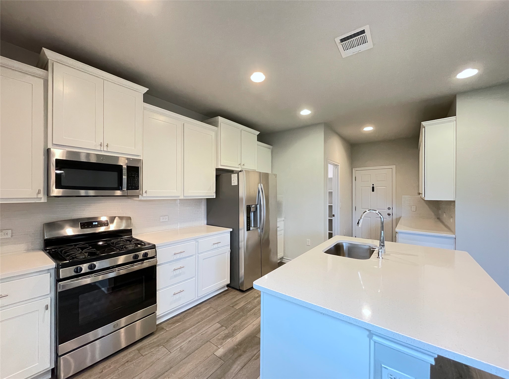 1602 Jacey Way Austin, TX 78725 - Photo 6 of 33 Modern kitchen featuring white cabinetry, light countertops, wood-finish flooring, and stainless steel appliances
