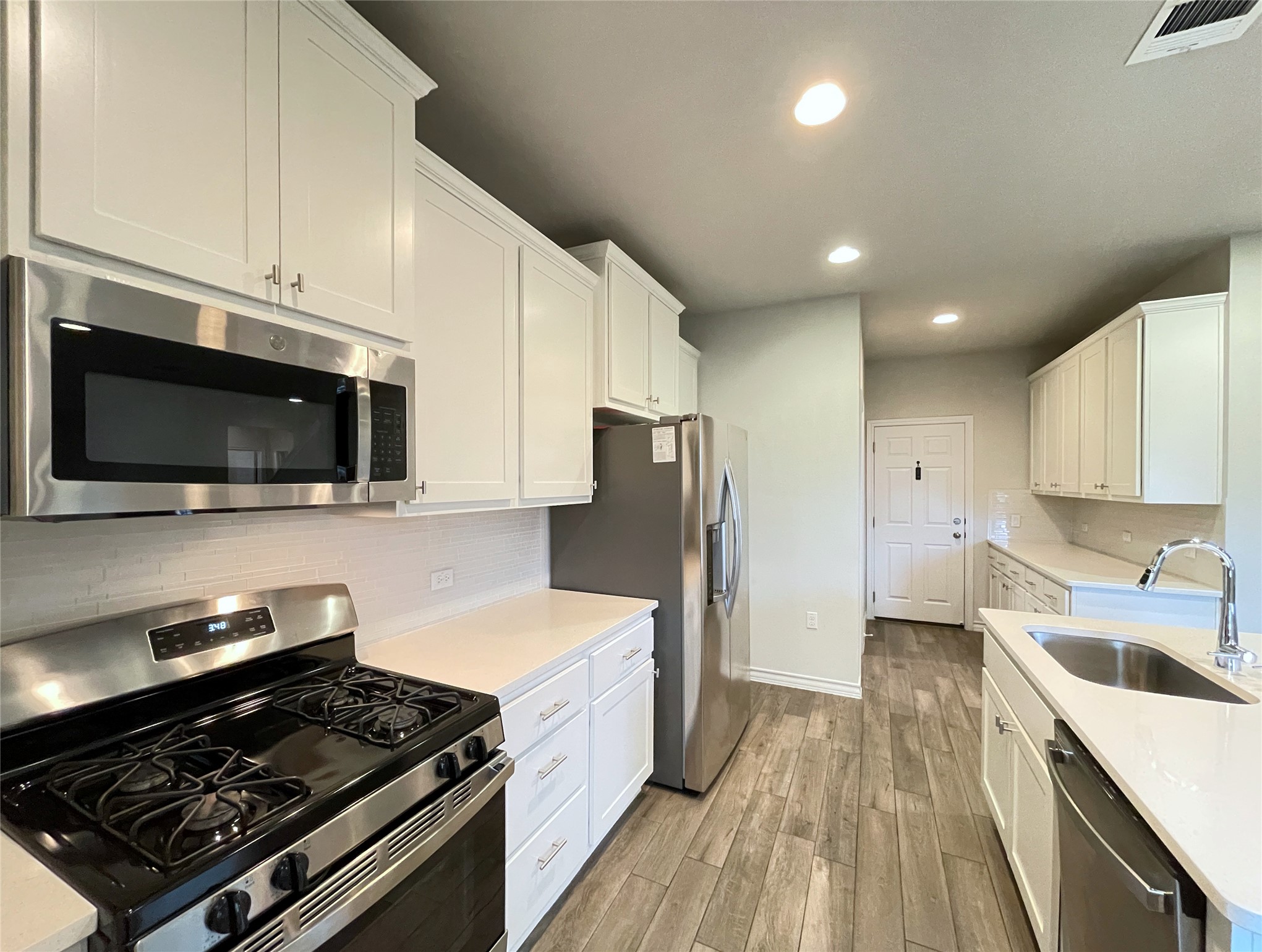 1602 Jacey Way Austin, TX 78725 - Photo 7 of 33 Well-appointed kitchen featuring white cabinetry, stainless steel appliances, wood-finish flooring, light-toned countertops, and a subway tile backsplash