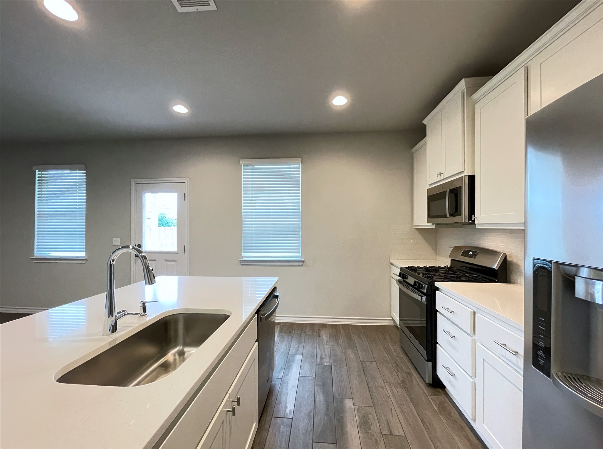 1602 Jacey Way Austin, TX 78725 - Photo 8 of 33 Kitchen featuring white cabinetry, stainless steel appliances, wood-finish flooring, recessed lighting, and an island with an undermount sink