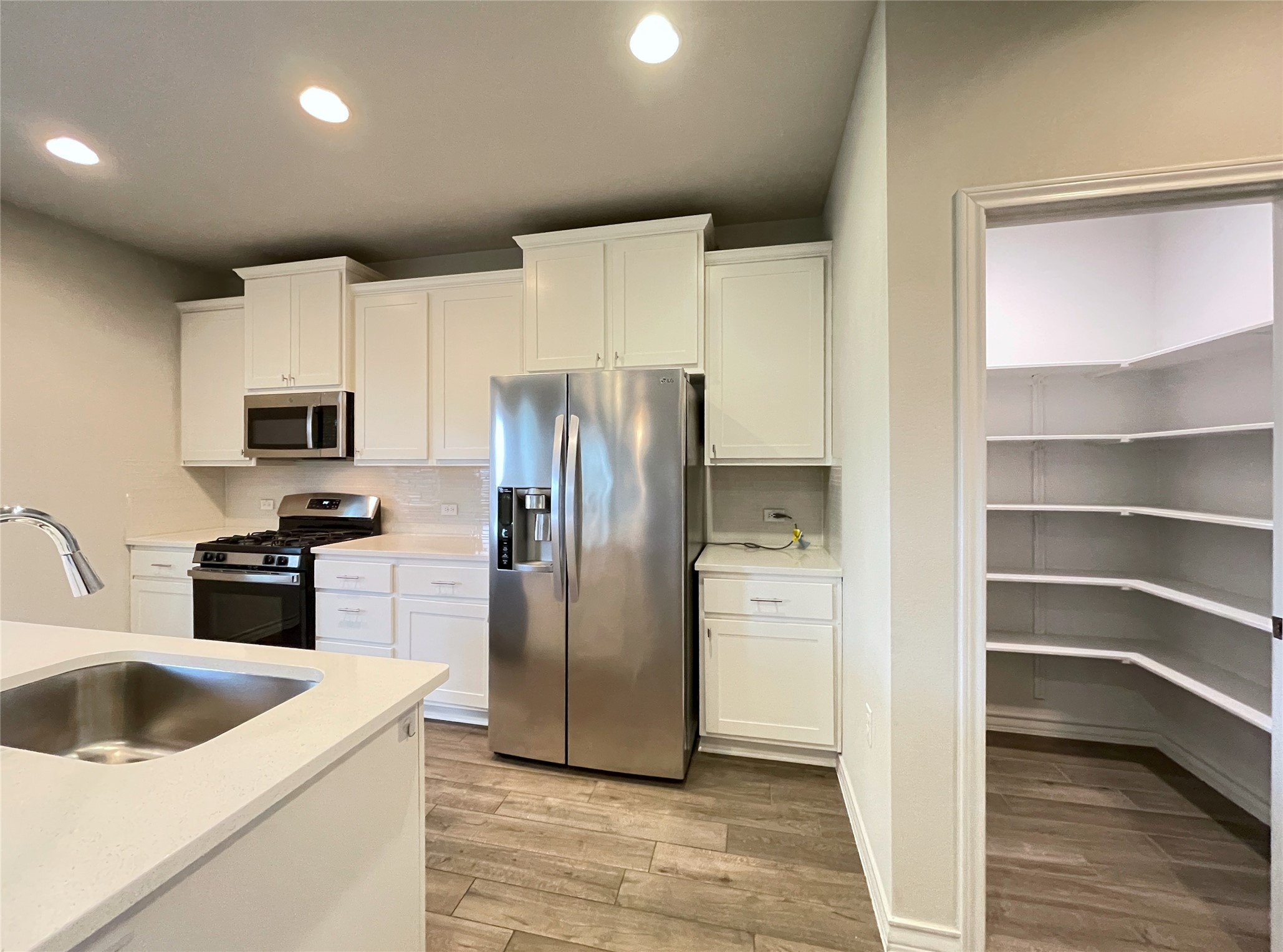 1602 Jacey Way Austin, TX 78725 - Photo 9 of 33 Modern kitchen featuring white cabinetry, stainless steel appliances including a refrigerator and gas range, light-toned countertops, and wood-finish flooring